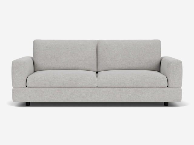 The Stage Track Sofa is a modern two-seater in light gray, featuring plush cushions and a minimalist design. It boasts square arms and a low-profile base, set against a plain white background.