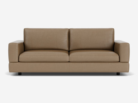 The Stage Track Sofa, featuring a minimalist design with thick cushions and square armrests, is showcased against a white background. Its brown leather upholstery and sleek, contemporary style are enhanced by short black legs.
