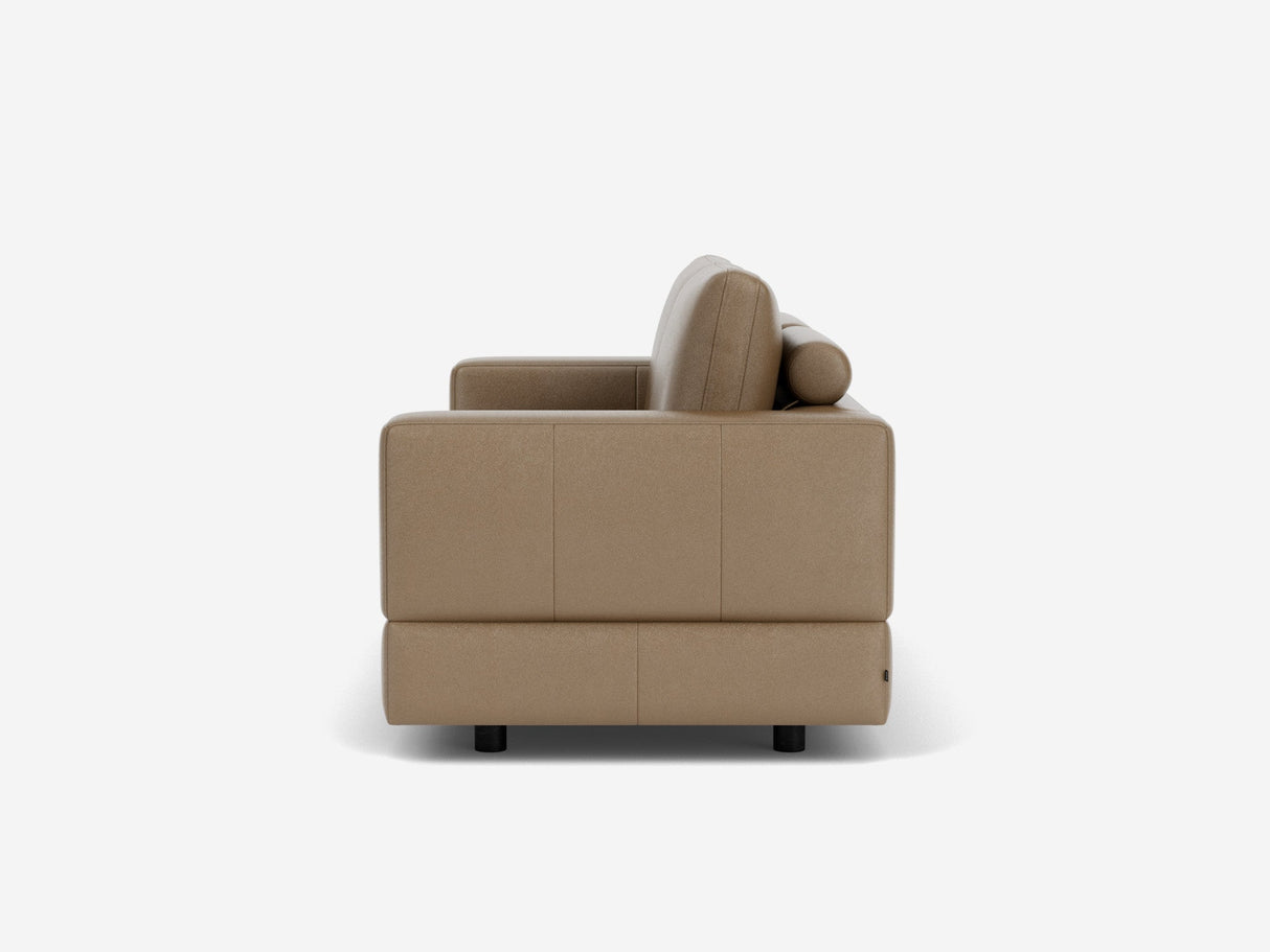 Side view of the Stage Track Sofa, featuring a modern beige design with square armrests and a cylindrical pillow, set against a plain white background. The sofa is elevated on small black legs.