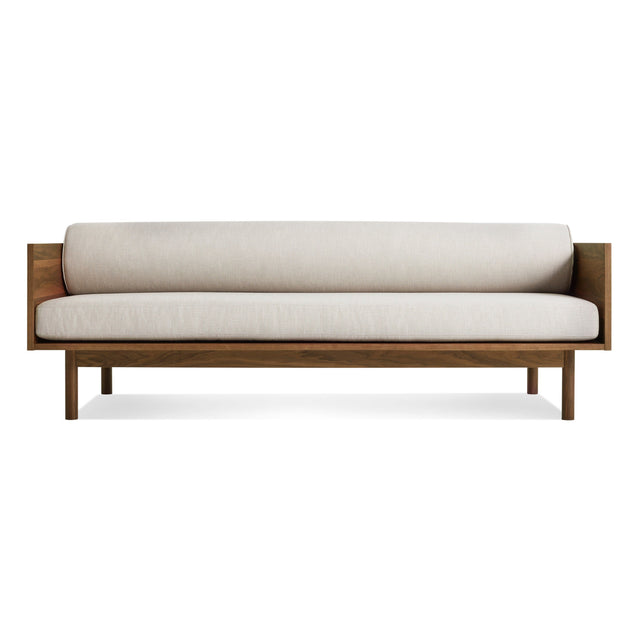 The Souvenir Sofa in Landa Stone with a walnut frame features minimalist design, clean lines, and light beige cushions, displayed against a plain white background.