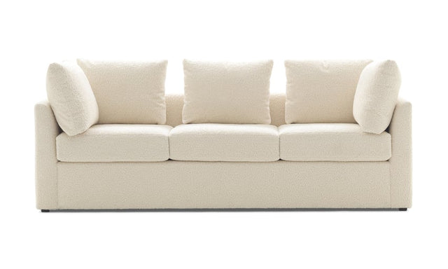 The Mitchell Gold + Bob Williams Dr Pitt Sofa is a modern, cream-colored, plush three-seater with clean lines and five matching cushions. Its minimalist design not only looks comfortable but also makes it ideal for a contemporary living room setting.